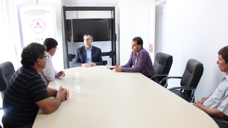 cinco homens sentados entorno de uma mesa de reunião.