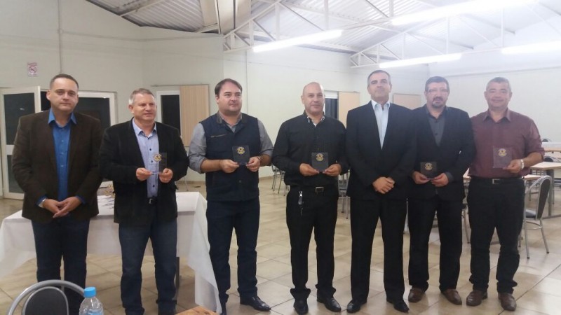 Homens lado a lado, segurando uma gratificação em forma de troféu, pelos anos trabalhados