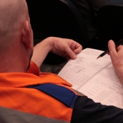 Um homem careca que usa laranja fazendo anotações em seu material