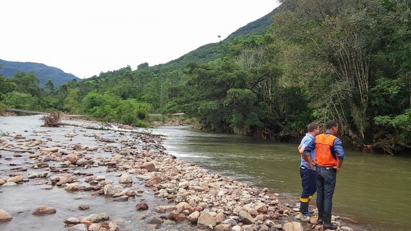 Dois homens vistoriando um área com água, pedras e mato.