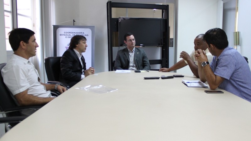 cinco homens em volta de uma mesa de reuni&atilde;o