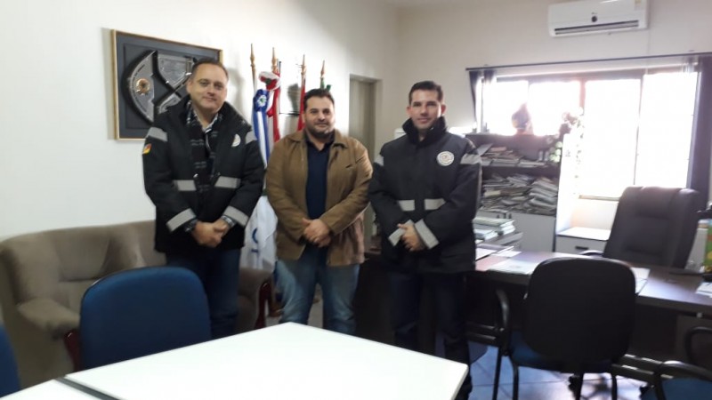 Três pessoas em pé com roupas escuras em uma sala bem iluminada.