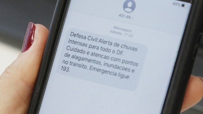 Celular, com mensagem sobre alerta de chuvas intensa com fundo branco.