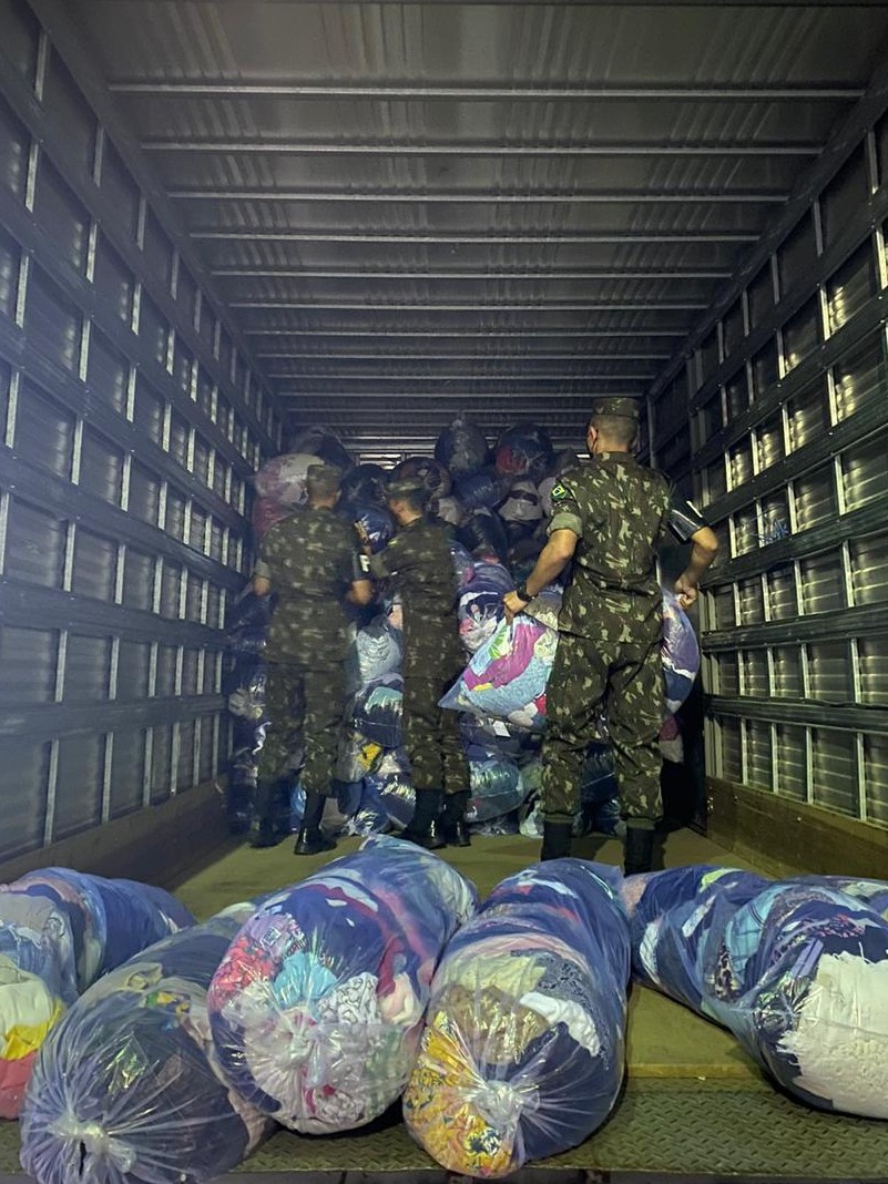 Caminhão tem três homens carregando kits de roupas.