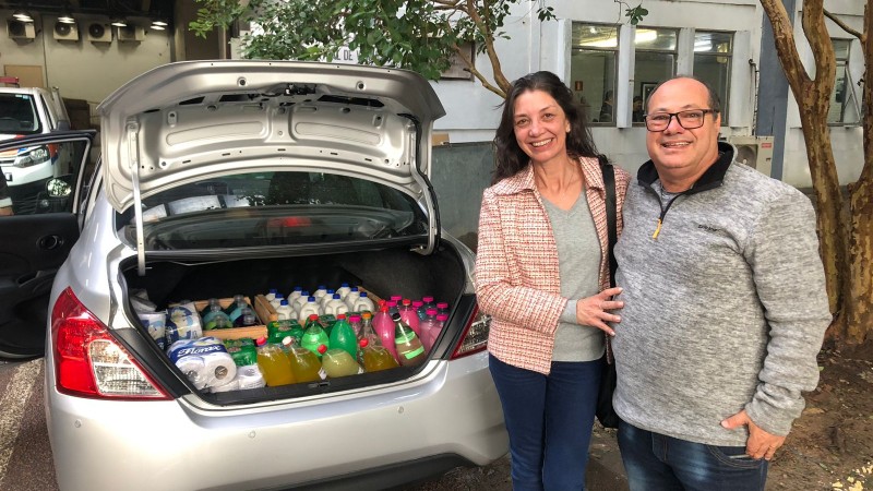 Casal Carlos e Simone ao lado do porta malas aberto de seu carro cinza com doações destinadas às vitimas do ciclone no RS