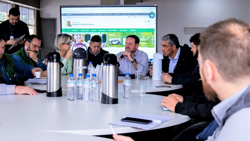 Imagem de várias pessoa sentadas à mesa em reunião.