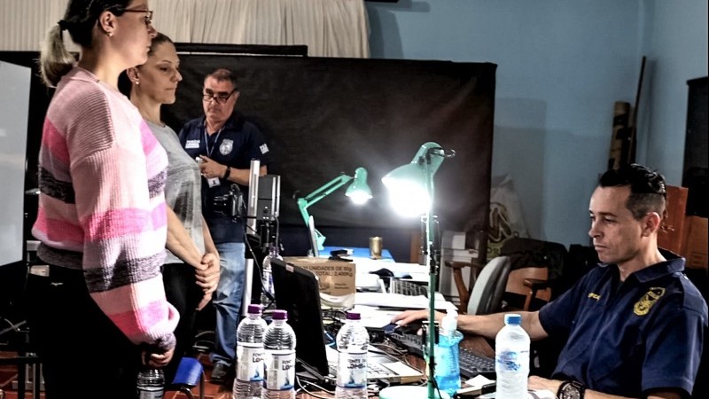Duas mulheres do lado esquerdo da imagem diante de uma mesa, onde um servidor do IGP, do lado direito da imagem, sentado, trabalha ao computador.