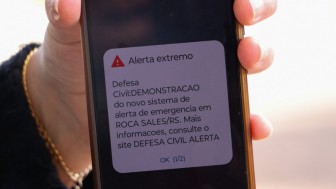 Uma pessoa segura um celular, no qual é possível ler Alerta extremo. Defesa Civil: demonstração do novo sistema de emergência em Roca Sales/RS. Mais informações consulte o site Defesa Civil Alerta