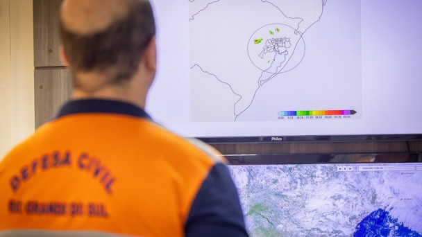 Representante da Defesa Civil de costas enquanto observa mapa do radar em tela