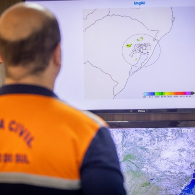 Representante da Defesa Civil de costas enquanto observa mapa do radar em tela