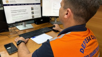 Representante da Defesa Civil à frente do computador enquanto acessa o site da Defesa Civil em página com o título transferência de recursos aos municípios fundo a fundo