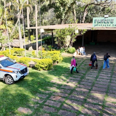espaço do parque zoologico com pessoas carregando sacolas para um encontro. consta uma viatura da defesa civil