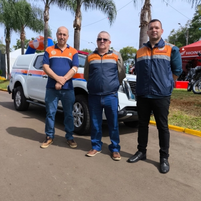 Três homens posando para foto em frente a viatura da defesa civil 