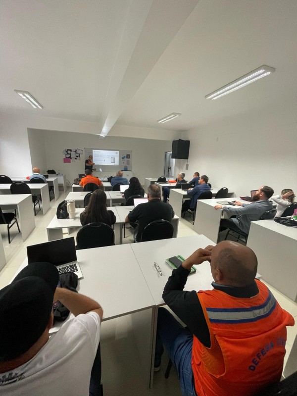 Participantes da capacitação assistem sentados em mesas à apresentação.