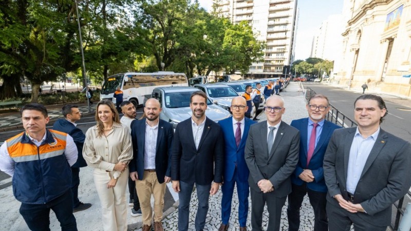 Grupo composto por representantes do MPSP, Defesa Civil e Governo RS posa para a foto, com uma fileira das novas viaturas ao fundo