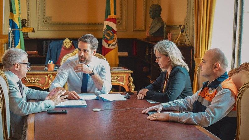 Quatro pessoas est&atilde;o sentadas ao redor de uma mesa, em reuni&atilde;o