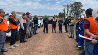 Um grupo de pessoas est&aacute; reunida em roda, em uma estrada de barro. &Eacute; poss&iacute;vel verificar pelas vestimentas que participam de diferentes &oacute;rg&atilde;os, como da Defesa Civil, da Brigada Militar e companhia de g&aacute;s.